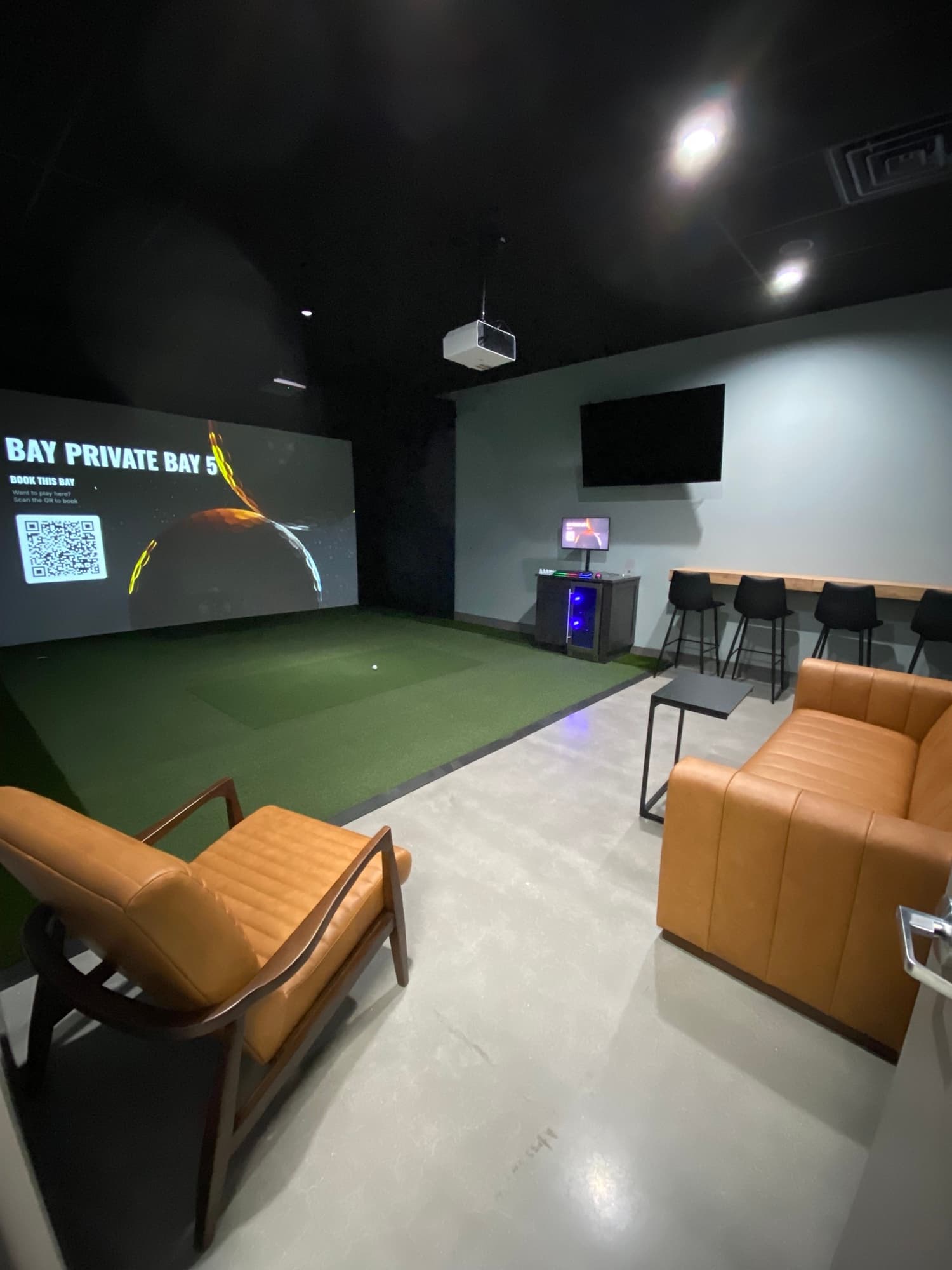 The private simulator bay at Unbound Golf, with seating and a screen