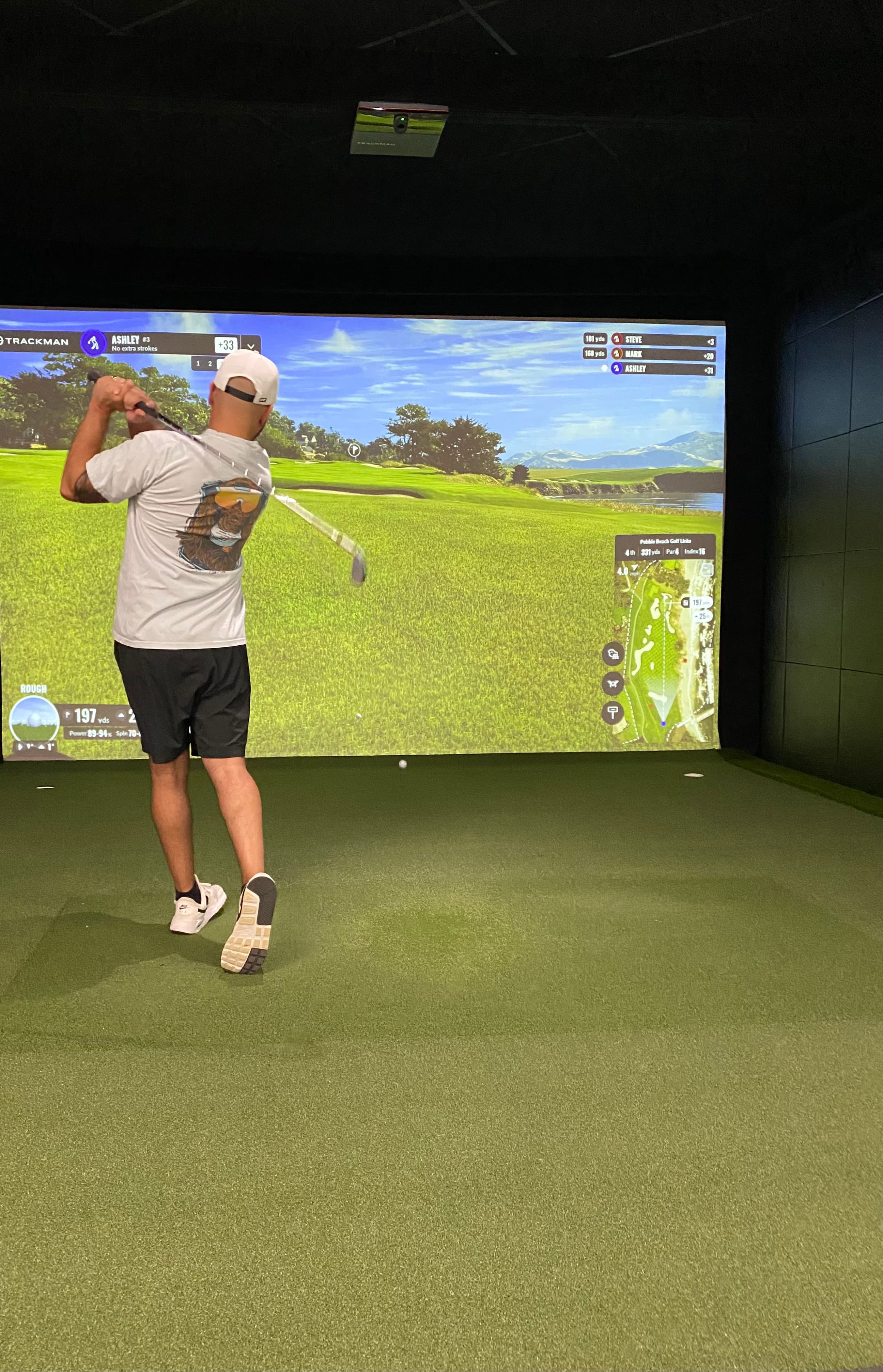 Golfer taking a swing in a Trackman simulator bay at Unbound Golf